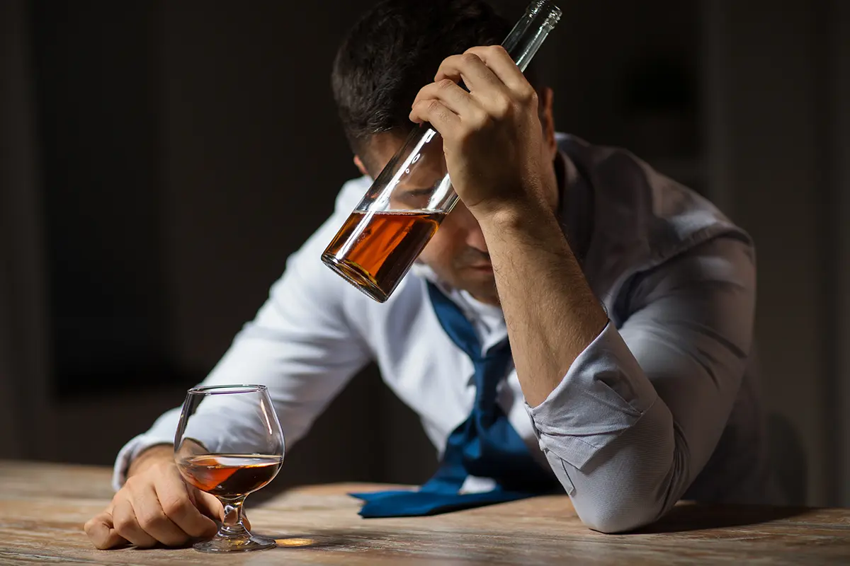 Ostatnie stadium alkoholizmu - zdjęcie ukazujące pijącego alkoholika siedzącego przy stole